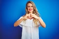 Young beautiful woman wearing white dress standing over blue isolated background smiling in love showing heart symbol and shape Royalty Free Stock Photo