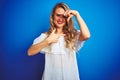 Young beautiful woman wearing white dress standing over blue isolated background smiling making frame with hands and fingers with Royalty Free Stock Photo