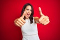 Young beautiful woman wearing white dress standing over red isolated background approving doing positive gesture with hand, thumbs Royalty Free Stock Photo