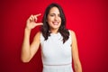 Young beautiful woman wearing white dress standing over red isolated background smiling and confident gesturing with hand doing Royalty Free Stock Photo