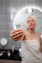 Young beautiful woman wearing white towel holding pink gouache scraper for face massage while doing beauty morning routine in Royalty Free Stock Photo