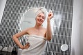 Young beautiful woman wearing white towel holding pink gouache scraper for face massage while doing beauty morning routine in Royalty Free Stock Photo