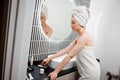 Young beautiful woman wearing white towel holding pink gouache scraper for face massage while doing beauty morning routine in Royalty Free Stock Photo