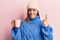 Young beautiful woman wearing winter clothes holding coffee smiling with an idea or question pointing finger with happy face, Royalty Free Stock Photo
