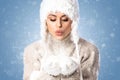 Young beautiful woman wearing winter hat and mittens over blue background, blowing snow with hands Royalty Free Stock Photo