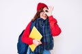Young beautiful woman wearing winter scarf and student backpack holding book smiling happy doing ok sign with hand on eye looking