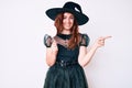 Young beautiful woman wearing witch halloween costume holding lollipop smiling happy pointing with hand and finger to the side Royalty Free Stock Photo