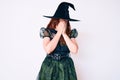 Young beautiful woman wearing witch halloween costume with sad expression covering face with hands while crying