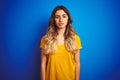 Young beautiful woman wearing yellow t-shirt over blue isolated background with serious expression on face Royalty Free Stock Photo