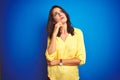 Young beautiful woman wearing yellow t-shirt standing over blue isolated background with hand on chin thinking about question, Royalty Free Stock Photo