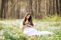 Young beautiful woman in a white dress collects primroses. A girl in the spring forest. A bouquet of white anemones in her hands Royalty Free Stock Photo