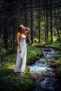 Young beautiful woman in white dress near icy stream on evergreen trees background in natural sunlight. Vertical image romantic Royalty Free Stock Photo