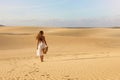 Young beautiful woman with white dress walking in the desert dunes  during sunset. Girl walking on golden sand on Corralejo Dunas Royalty Free Stock Photo