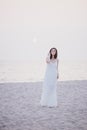 Young beautiful woman in a white dress walking on an empty beach near ocean Royalty Free Stock Photo