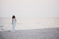 Young beautiful woman in a white dress walking on an empty beach near ocean Royalty Free Stock Photo