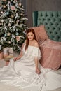 Young beautiful woman in white elegant evening dress sitting on floor near christmas tree and presents. Interior with christmas de Royalty Free Stock Photo