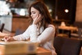 Young beautiful woman in white jacket taking notes to her planner working outside office drinking hot coffee in the trendy cafe Royalty Free Stock Photo