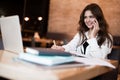 Young beautiful woman in white jacket working in her laptop taking notes in her planner while drinking hot coffee in the cafe Royalty Free Stock Photo