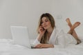 Young beautiful woman in white shirt relaxing on the bed using laptop computer in the bedroom. Working from home. Royalty Free Stock Photo