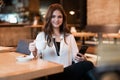 Young beautiful woman in white stylish blouse drinking coffee and checking her phone after hard workday sitting in cafe modern