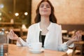 Young beautiful woman in white stylish blouse drinking hot coffee after hard workday sitting in peaceful position relaxing in