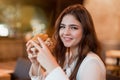 Young beautiful woman in white stylish blouse eating meat burger for lunch in trendy cafe looking happy eating outside Royalty Free Stock Photo