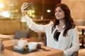 Young beautiful woman in white stylish blouse looks shoots selfie while having meat burger with fries for lunch in trendy cafe Royalty Free Stock Photo