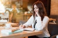 Young beautiful woman in white stylish jacket working on project outside office writing in planner during coffee break in cafe Royalty Free Stock Photo