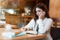 Young beautiful woman in white stylish jacket working on project outside office writing in planner during coffee break in cafe Royalty Free Stock Photo