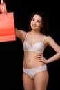 A young beautiful woman in white underwear with a red paper shopping bag poses and smiles. on a black isolated background Royalty Free Stock Photo