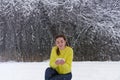 A young beautiful woman in winter in a bright yellow sweater holds snow in her hands and looks at it. Lady in the snowy forest for Royalty Free Stock Photo