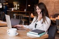 Young beautiful woman working in her laptop having phone conversation while drinking hot coffee in the cafe multitasking modern Royalty Free Stock Photo