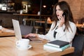 Young beautiful woman working in her laptop looking surprised during phone conversation while drinking hot coffee in the cafe Royalty Free Stock Photo