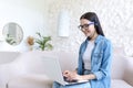 Young beautiful woman working at home sitting on sofa, using headset and laptop for video call Royalty Free Stock Photo