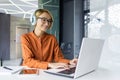 Young beautiful woman working on laptop inside office at workplace, smiling businesswoman listening to online podcast Royalty Free Stock Photo