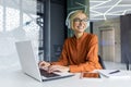 Young beautiful woman working on laptop inside office at workplace, smiling businesswoman listening to online podcast Royalty Free Stock Photo