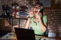 Young beautiful woman working at the office at night speaking on the phone shouting and screaming loud to side with hand on mouth Royalty Free Stock Photo