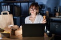 Young beautiful woman working using computer laptop and eating delivery food looking sleepy and tired, exhausted for fatigue and Royalty Free Stock Photo