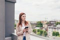 Young beautiful woman writes on the phone, standing on the balcony of the office center Royalty Free Stock Photo