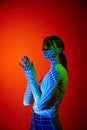 Young beautiful woman's portrait with digital neon filter lights on body over red background. Concept of art Royalty Free Stock Photo