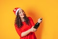 Young beautiful woman on yellow background, on her head she has santa hat. Woman holding bottle in her hands and opening the Royalty Free Stock Photo