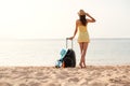 Young beautiful woman in yellow dress and hat with large suitcase on tropical beach. Girl look on sea Royalty Free Stock Photo