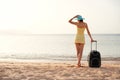 Young beautiful woman in yellow dress and hat with large suitcase on tropical beach. Girl look on sea Royalty Free Stock Photo