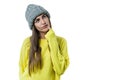 Young beautiful woman in yellow sweater and gray big loop knitted beanie hat, thoughtful holding a finger near her lips, on white Royalty Free Stock Photo