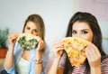 Young beautiful women eating slices of tasty Italian pizza at home - Happy pretty sisters covering their faces with fast food
