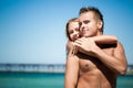 Young beautiful woman embracing and kissing from back her smiling boyfriend with blue sea and sandy beach at background Royalty Free Stock Photo