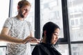 Young beautiful woman having her hair cut at the hairdresser`s. Young male hairdresser smiling and making hairstyle to Royalty Free Stock Photo