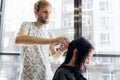 Young beautiful woman having her hair cut at the hairdresser`s. Young male hairdresser smiling and making hairstyle to Royalty Free Stock Photo