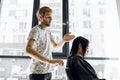 Young beautiful woman having her hair cut at the hairdresser`s. Young male hairdresser smiling and making hairstyle to Royalty Free Stock Photo