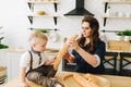 Young beautiful woman in the kitchen giving a baguette to her pretty little son Royalty Free Stock Photo